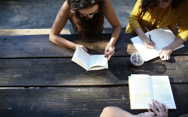 Drei Studierende lesen und lernen im Sonnenschein an einem Gartentisch.