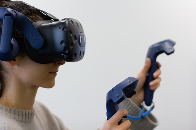 Eine Frau mit einer VR-Brille die zwei Controller vor sich ausstreckt