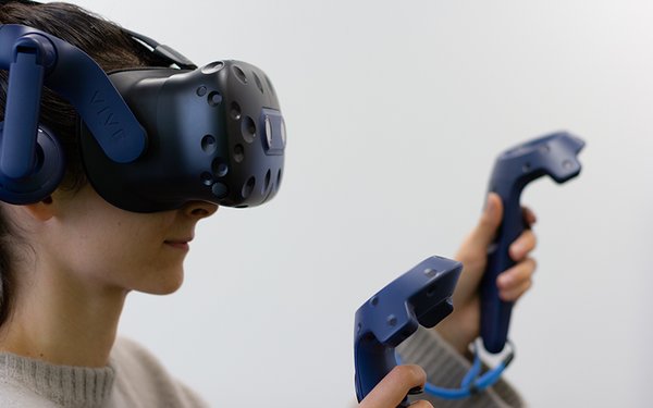 Eine Frau mit einer VR-Brille die zwei Controller vor sich ausstreckt