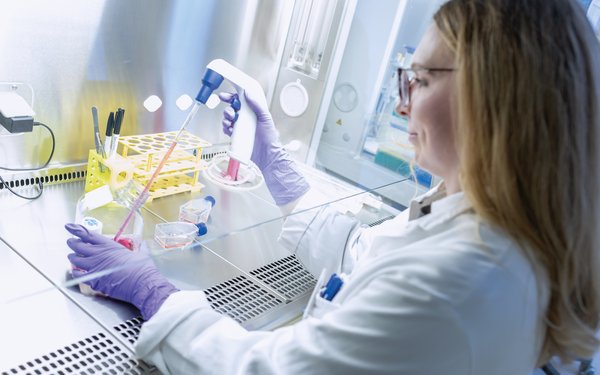 Victoria Fincke steht in Laborkleidung an einem Labortisch und hantiert mit einem Versuchsaufbau.