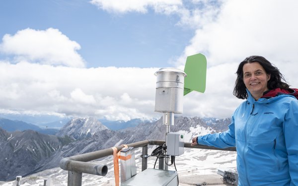 Prof. Dr. Claudia Traidl-Hoffmann steht in einer blauen Winterjacke auf der Zugspitze. Neben ihr gro?e Messger?te, im Hintergrund Bergpanoramma.