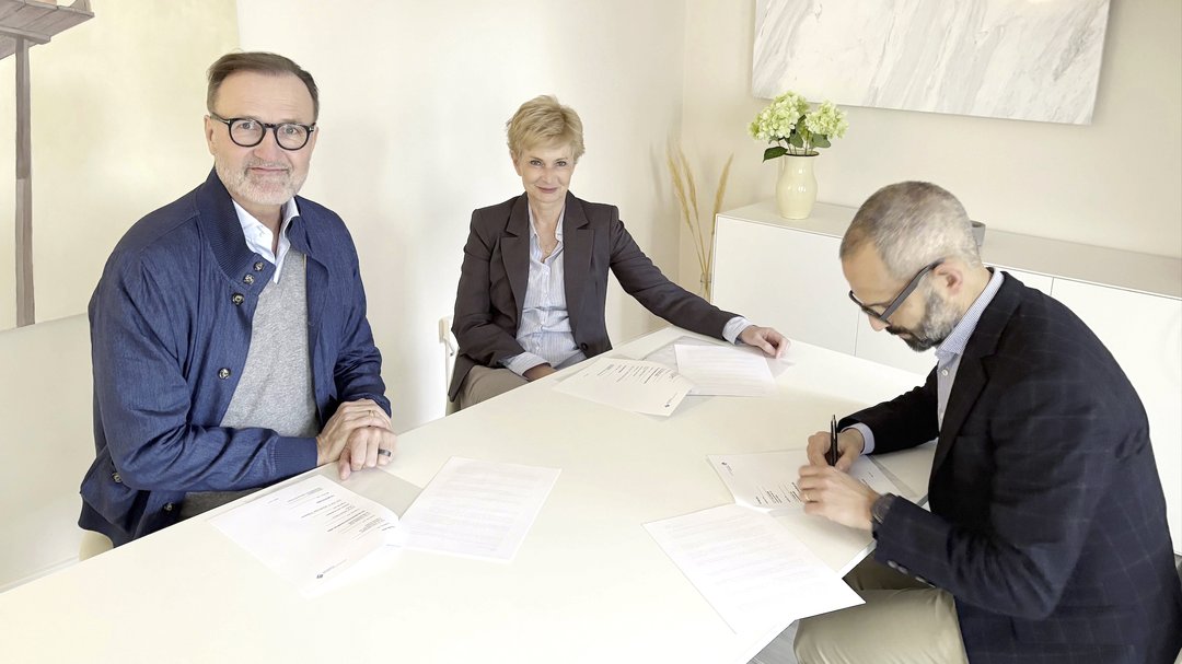 Jan Fischer und Carolina Milberg sitzen an einem Tisch und lächeln in die Kamera. Prof. Dr. Alkomiet Hasan unterzeichnet einen Vertrag.