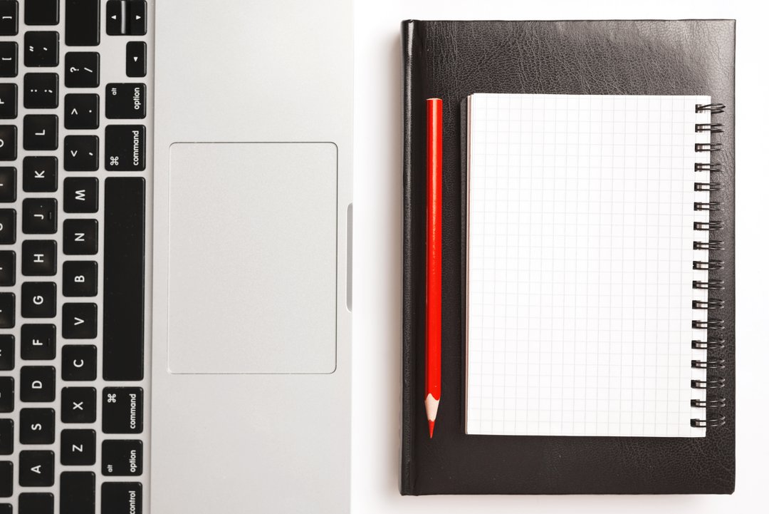 A laptop with notebook and red pencil
