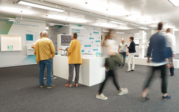 Mehre Personen unterhalten sich bzw laufen durch den Showroom. Zentral ist das Ausstellungsstück "Getriebedemonstrator" zu sehen.