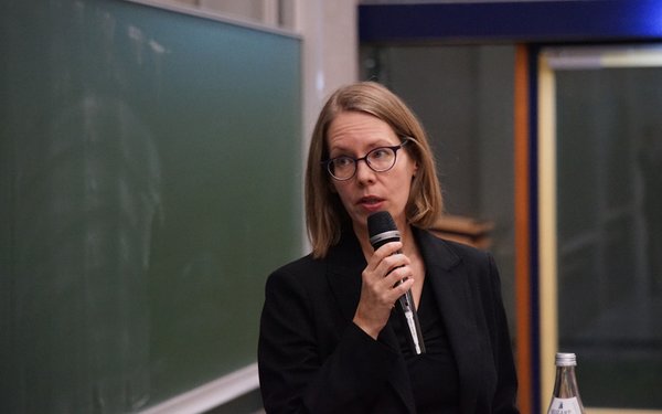 Frau Brorhilker steht mit einem Mikrofon in der Hand vor einer grünen Tafel.
