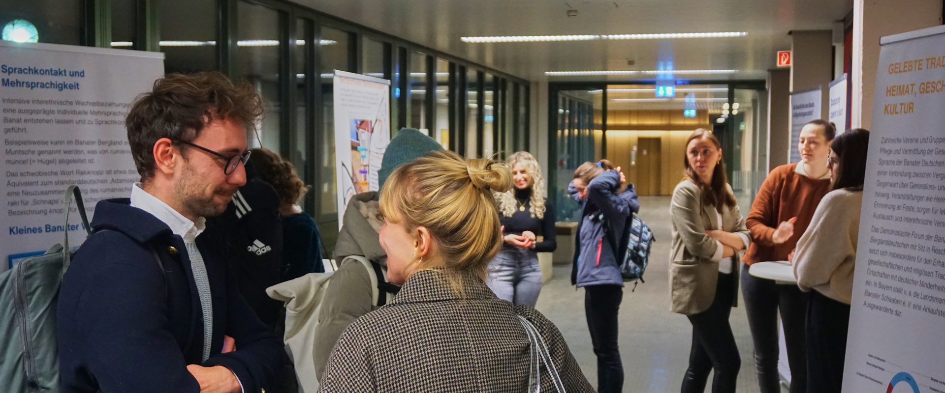 Besucher:innen stehen vor verschiedenen Stellwänden und unterhalten sich mit den Autor:innen der jeweiligen Roll-Up-Banner.