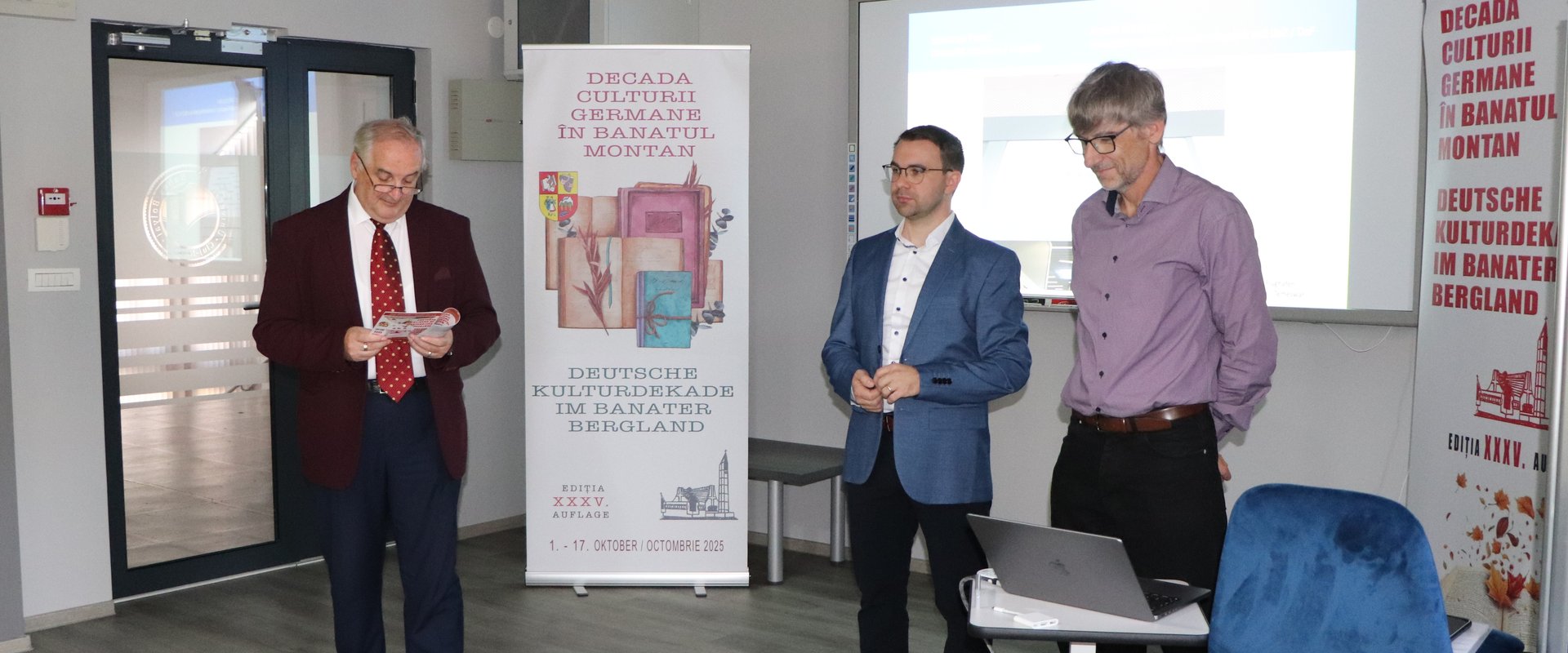 Es sind Herr Tigla, Herr Franz und Herr Wildfeuer vor der Präsentation stehend zu sehen.