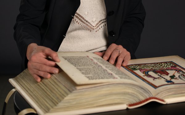 Anna Kathrin Bleuler mit Faksimile des Codex Manesse, der mittelalterlische Literatur und Bilder zeigt.