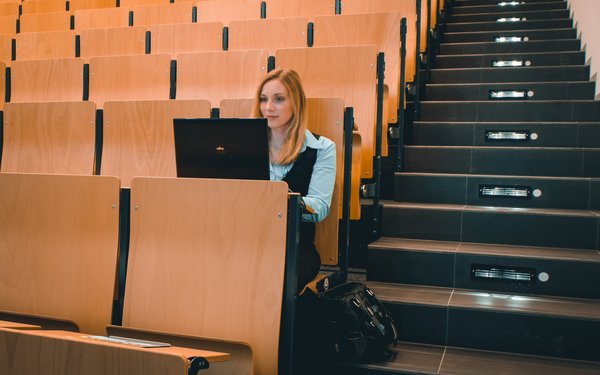 Studentin sitzt alleine mit Laptop im Hörsaal