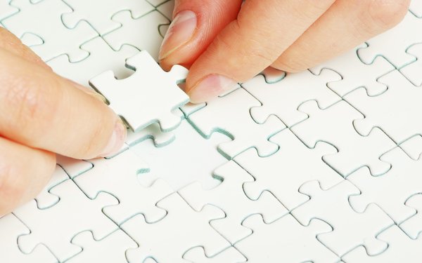 Mit jeweils zwei Fingern wird das fehlende Puzzleteil gerade in die passende Lücke eingesetzt. Das Puzzle soll symbolisch für die an der Inklusion beteiligten Institutionen stehen.