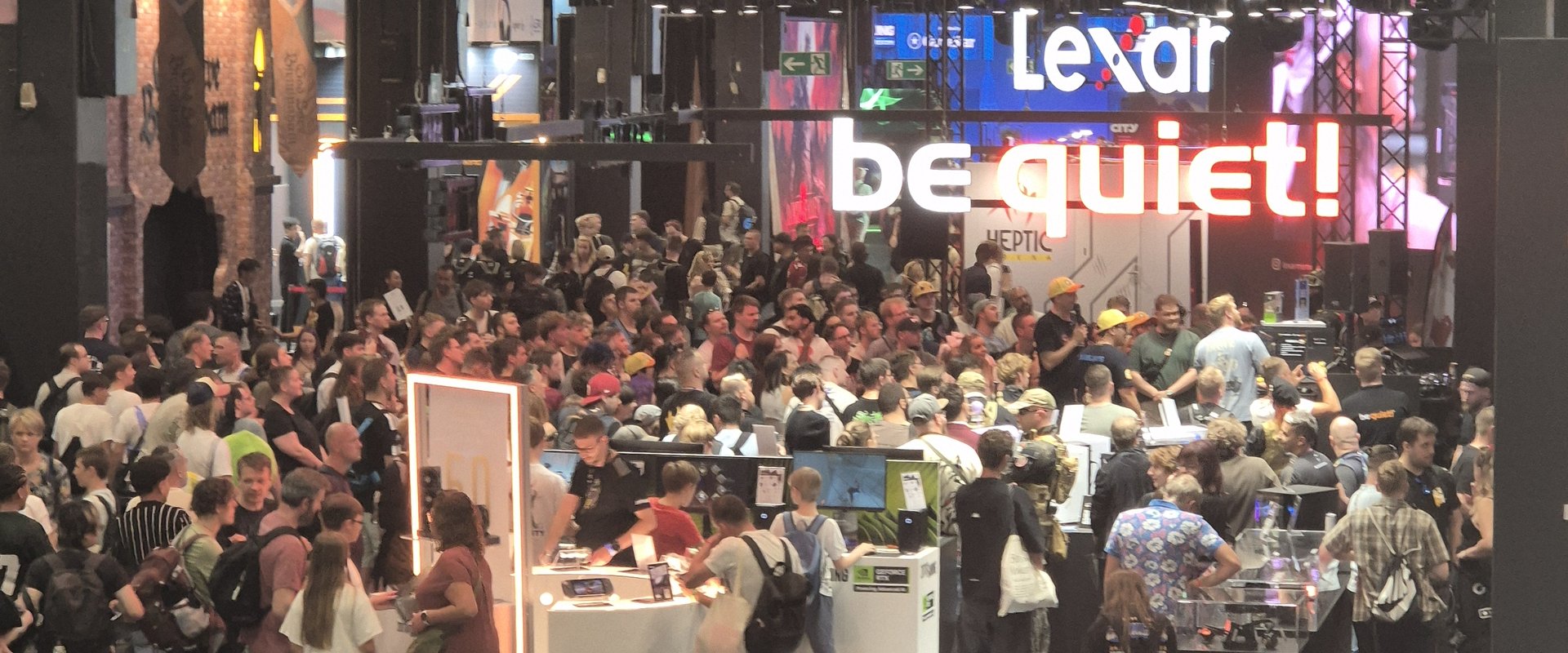 View of the exhibition hall. People are gathered around exhibition stands. In the background is a large, colourful screen.