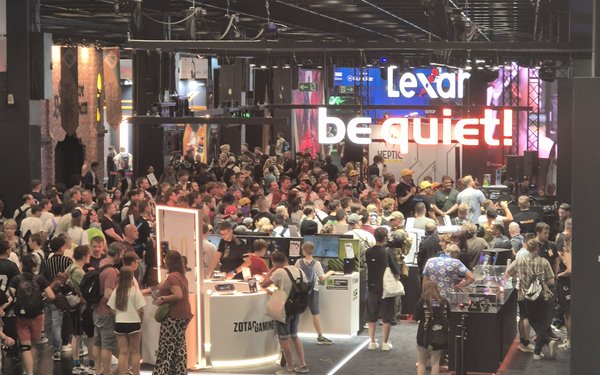 Blick in die Messehalle. Menschen gruppieren sich um Messestände. Im Hintergrund eine große, bunte Leinwand.