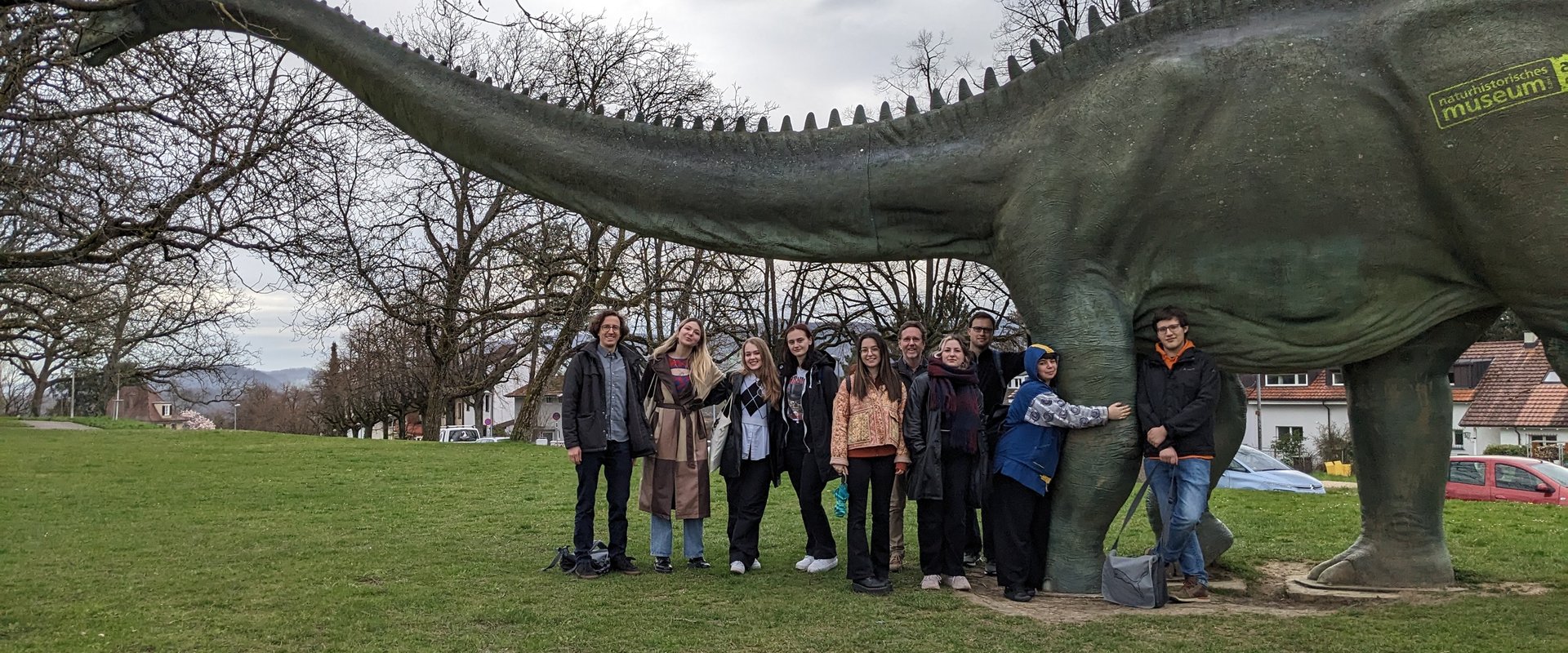 Eine Gruppe aus 10 Menschen vor einer Dinosaurierfigur im Freien