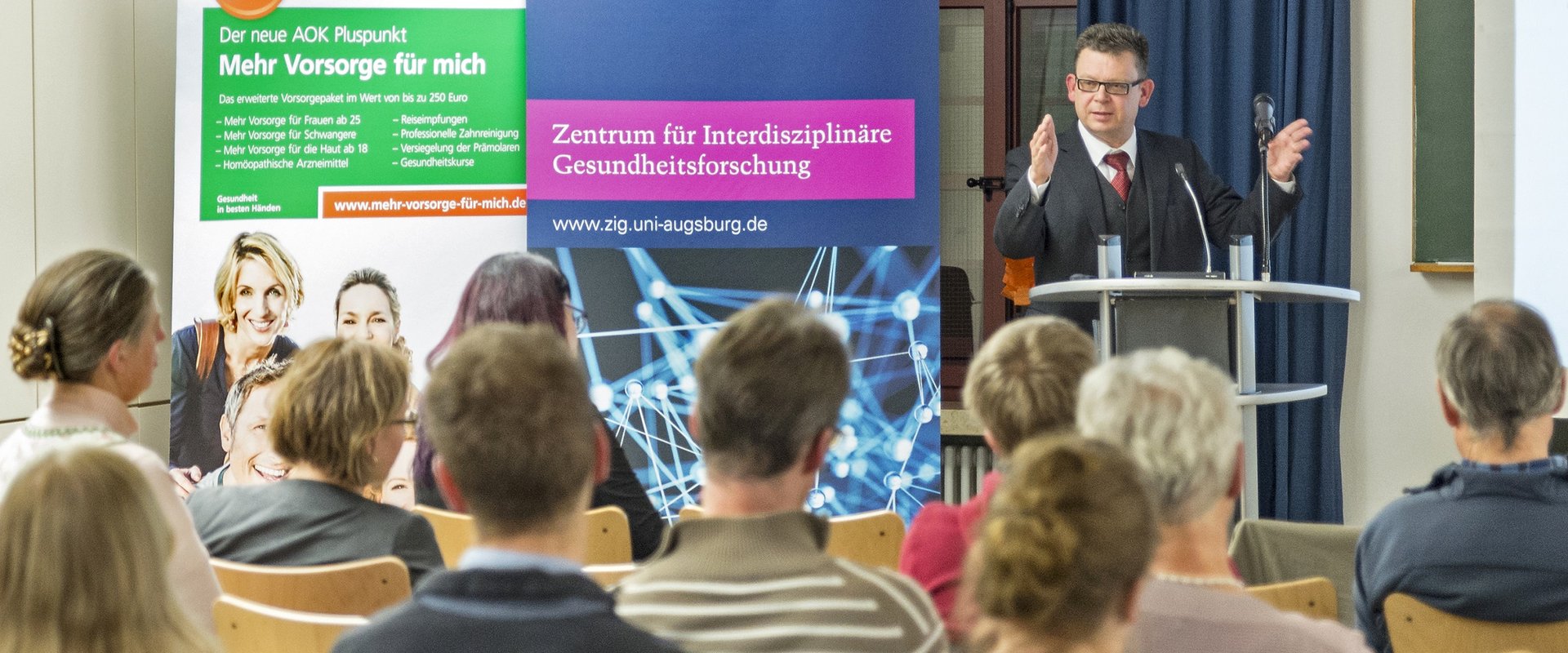 Das Bild zeigt den Redner und das Publikum beim 1. AGD