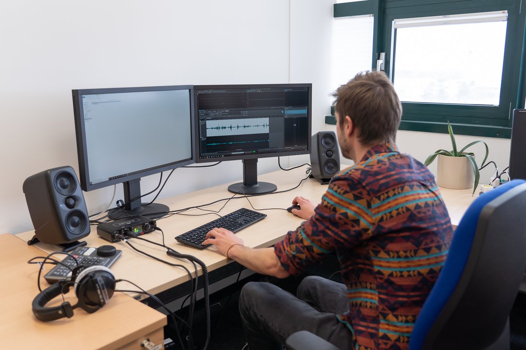 Person vor zwei Bildschirmen, diese zeigen Audioschnitt-Programme