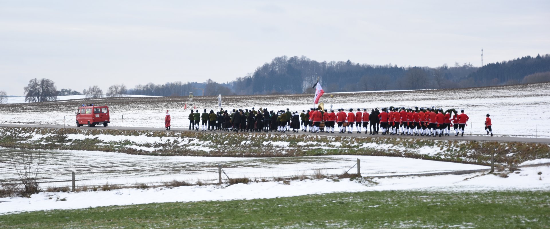 Eine Gruppe von rot-schwarz gekleideten Dinkelscherbener Sch?fflern geht auf einer Stra?e, die Landschaft ist Schnee bedeckt