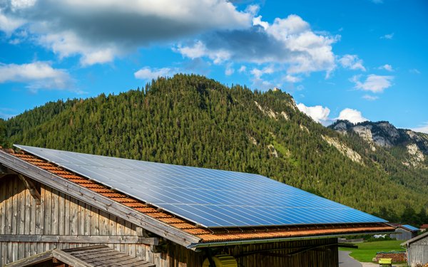 Scheune mit PV-Anlage auf dem Dach, im Hintergrund Berge