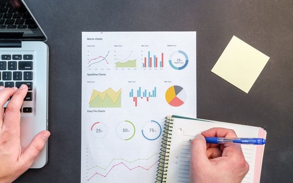 Blick auf die Hände eines Büroarbeiters mit Laptop, Stift, Block und Diagrammen