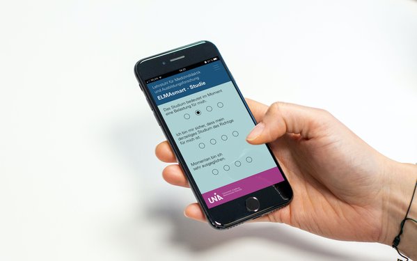 Hand, die Smartphone hält, auf welchem ein Umfragetool zu sehen ist.