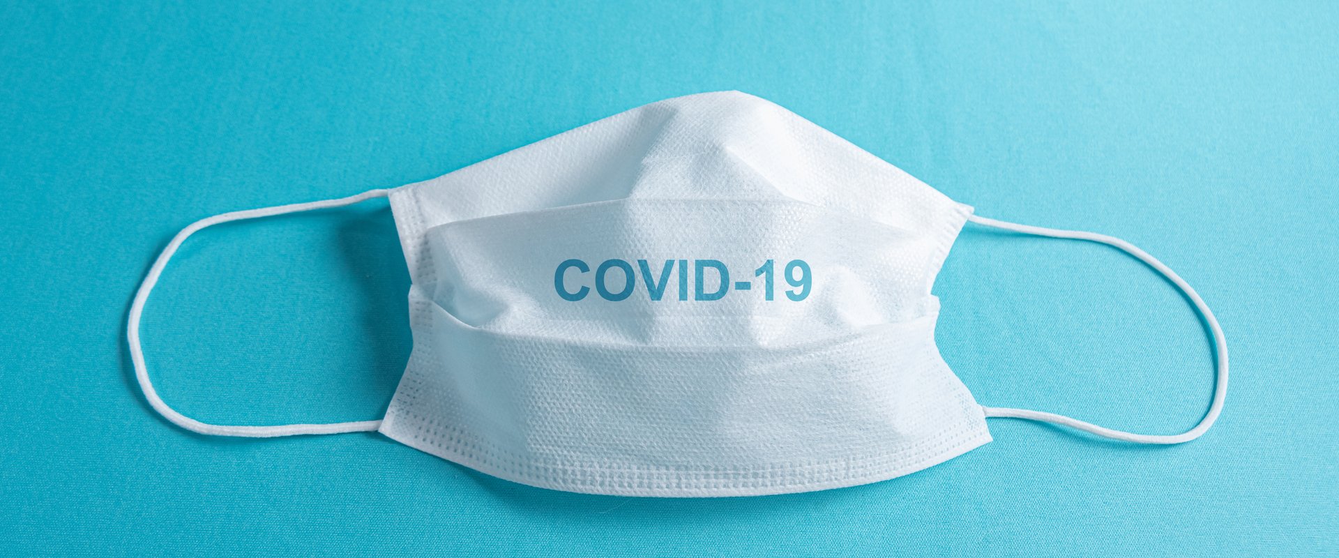 OP Maske auf blauen Untergrund mit einem COVID-19 Schriftzug