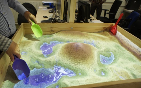 Kleiner Sandkasten, auf den virtuell die Topografie einer Landschaft projiziert ist.