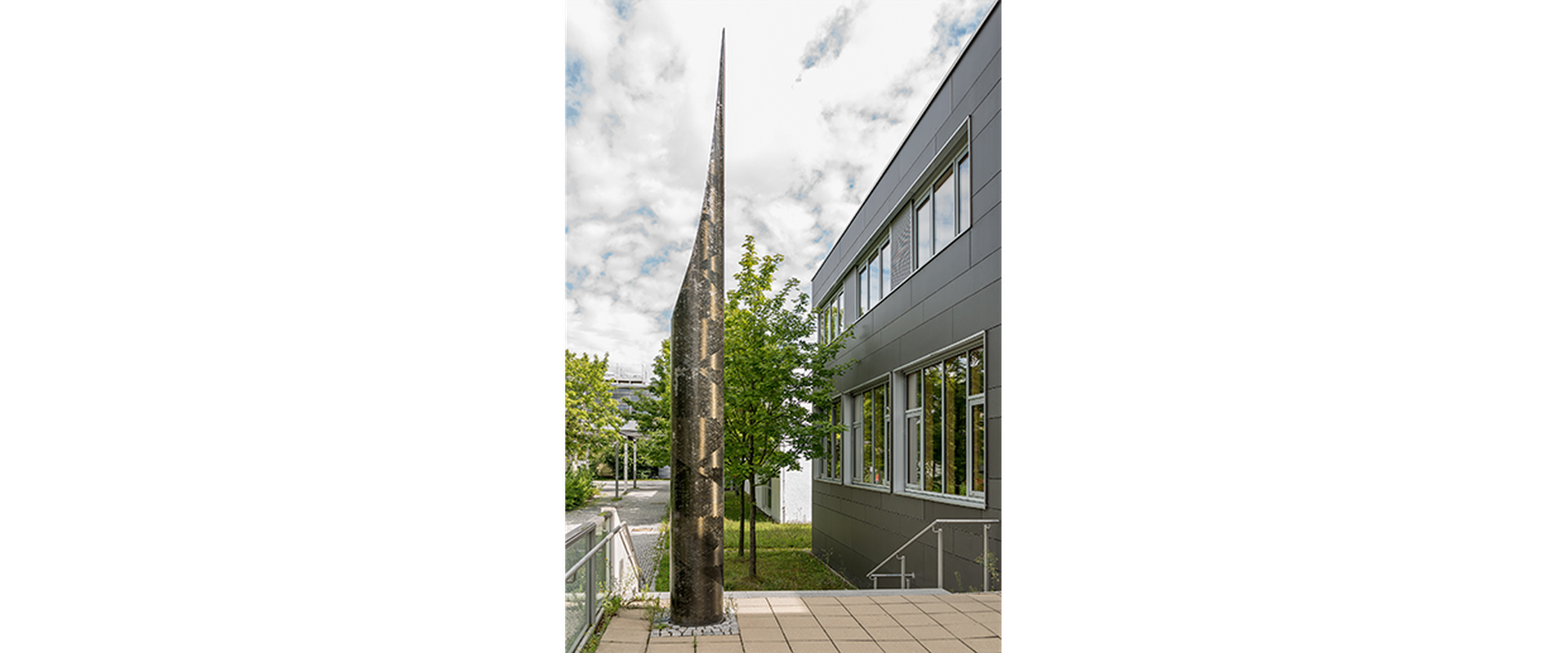 Auf dem Bild sieht man das Kunstwerk Pip vom Künstler Robert Kessler. Es stellt eine silberene Säule, die nach oben spitz zuläuft, dar.