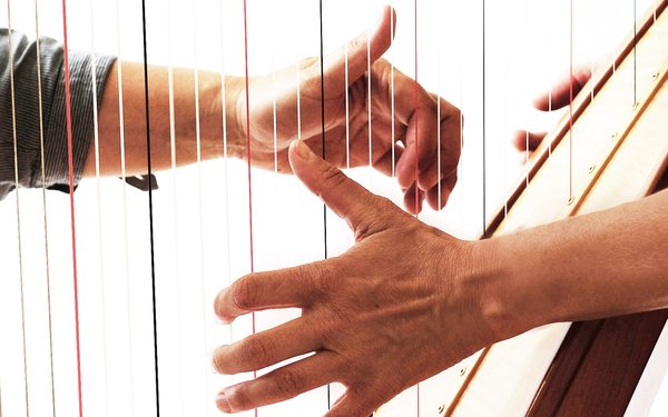 Hände von zwei Personen, die auf einer Harfe gemeinsam spielen