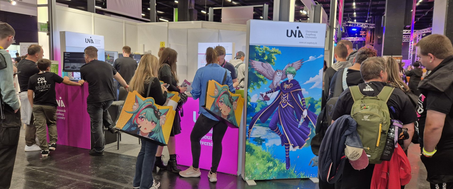 The University of Augsburg's exhibition stand. Several people are standing in front of it, gathering information.