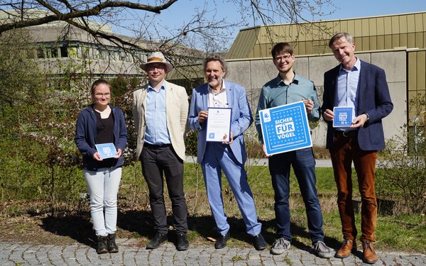 F��nf Personen posieren f��r ein Foto nach der Aush?ndigung der Urkunde f��r eine Vogelfreundliche Glasfl?che vom LBV an die Universit?t Augburg.