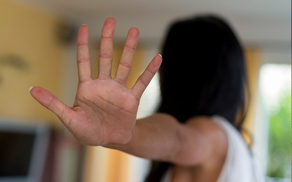 Im Zentrum des Bildes sieht man eine ausgstreckte Hand, die in einer Abwehrhaltung, ein Stop symbolisiert. Im Hintergrund sind die Umrisse einer schwarzhaarigen Person zu erkennen.