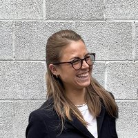 Examenskandidatin Johanna in Portraitaufnahme vor einer grauen Mauer. Sie ist im Gespräch und lacht.
