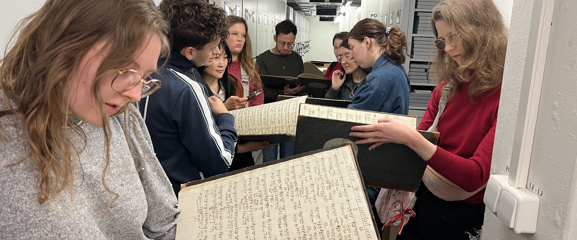 Es sind die Studierenden zu sehen, wie sie im Archiv der Akademie der Wissenschaften alte Dokumente ansehen.