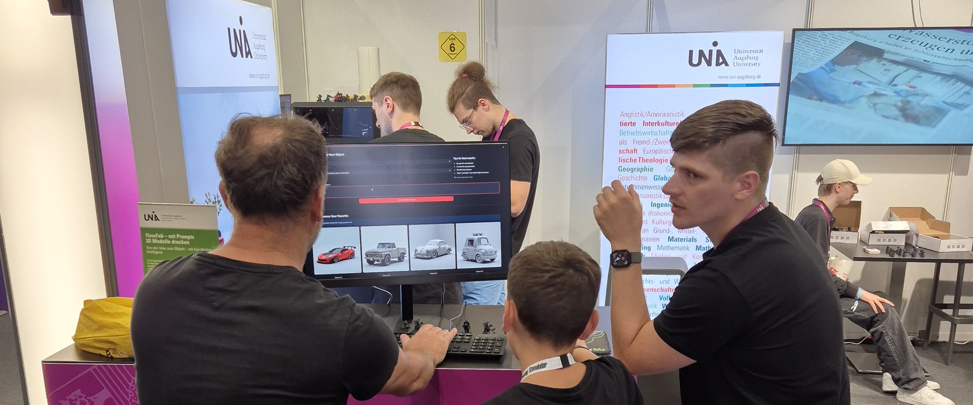 Three people are standing in front of computers in the foreground, while two others are working on the 3D printer in the background.