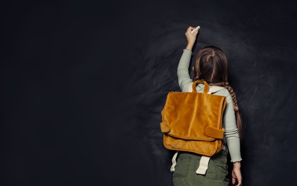 Kind mit Schulrucksack schreibt an eine Tafel