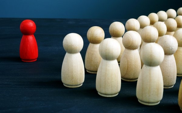 Eine rote Spielfigur steht mehrern weißen Spielfiguren gegenüber.