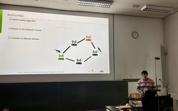 Bild zeigt Thomas B?hme hinter einem Rednerpult auf der linken Seite. Zudem ist eine Folie aus der Pr?sentation hinter der Person zu sehen.